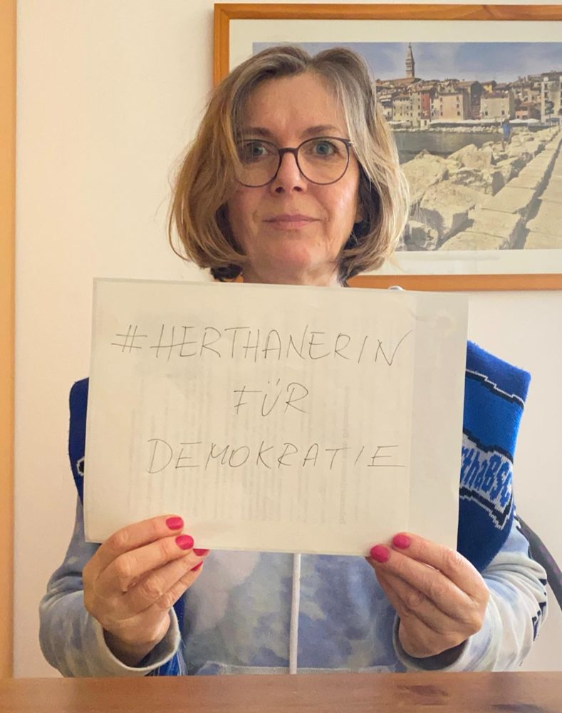 Hertha-Fan im Hertha-Outfit mit Schild in der Hand, auf dem steht: Herthanerin für Demokratie