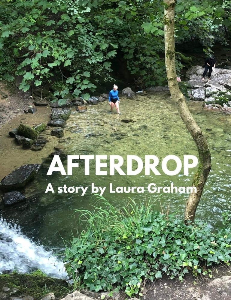 A woman in a swimming costume stands at the edge of a natural pool. She is walking into the water. 
