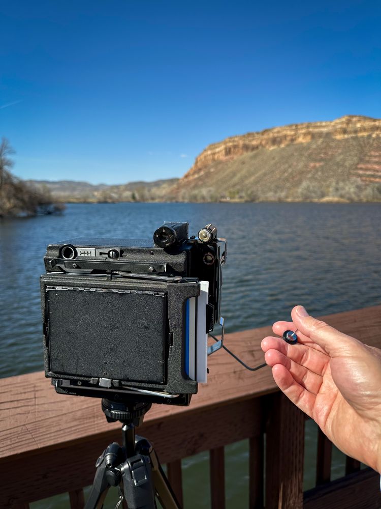 In a close-up photo, I'm standing on a dock, the film holder is loaded in a Crown Graphic 4x5, and my hand is holding a short shutter release cable, ready to take a photo of Watson Lake. 