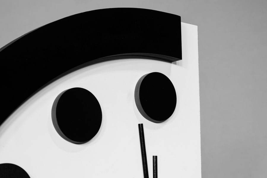 An image of the top of a stylized analog clock, the Doomsday Clock, with a wide black border on top, solid black circles instead of numbers, and the tops of the minute and hour arms visible, close to midnight.