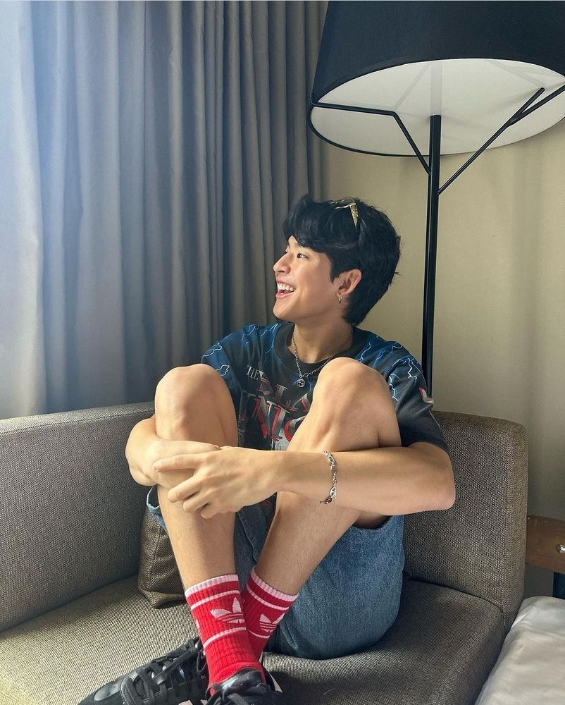 Mark Pakin sitting on a sofa with his arms wrapped around his knees, looking to the right and smiling