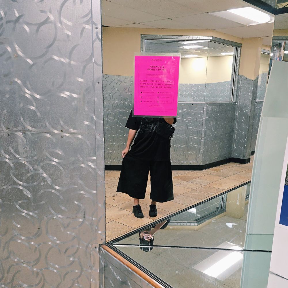 mirror selfie in 24 hour fitness with a bigass pink sign blocking my face & im wearing big pant, black seventeen [new_] tour shirt & all black adidas shell toes 