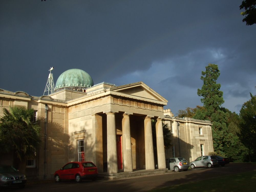 The historic Institute of Astronomy Cambridge building against a stormy sky. Rising from the roof is the dome of the observatory.