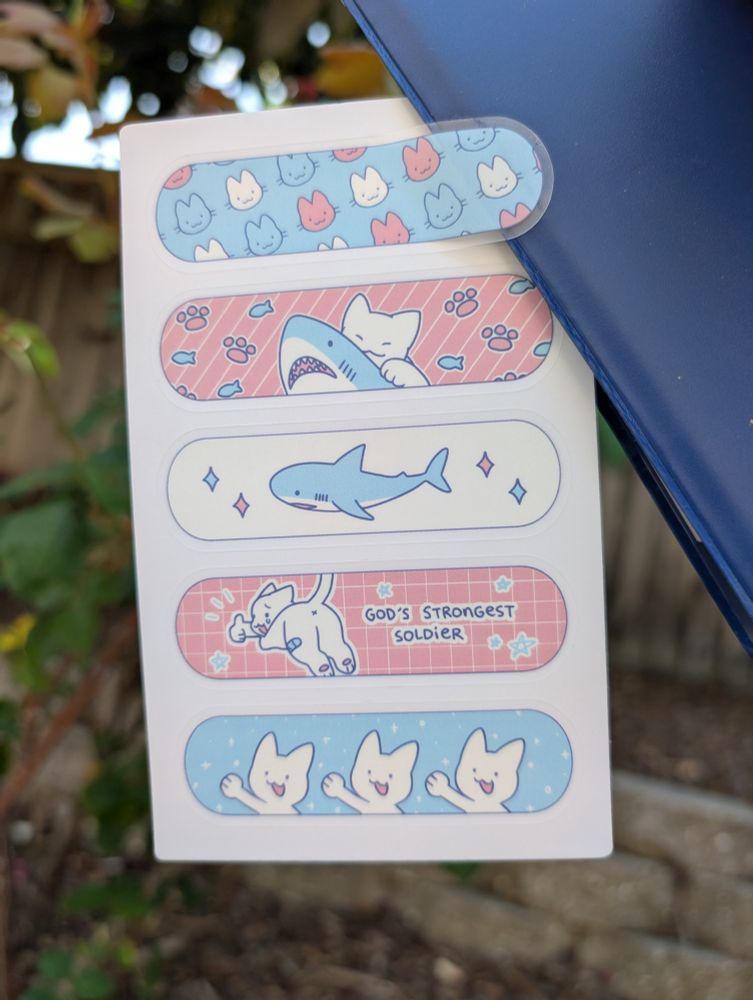 image of sticker sheet, 5 stickers featuring cats and sharks printed in trans colors