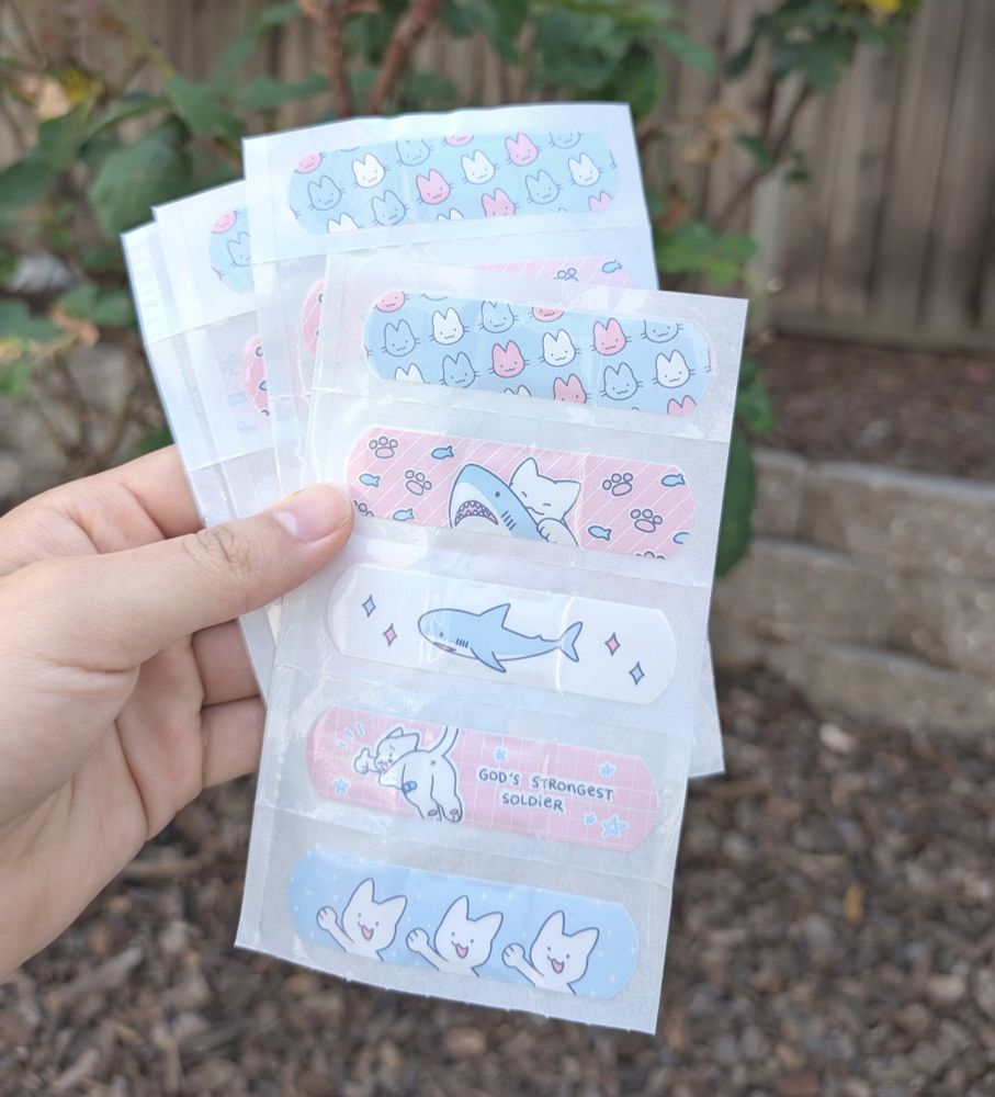 image of bandage sheet, 5 bandages featuring cats and sharks printed in trans colors
