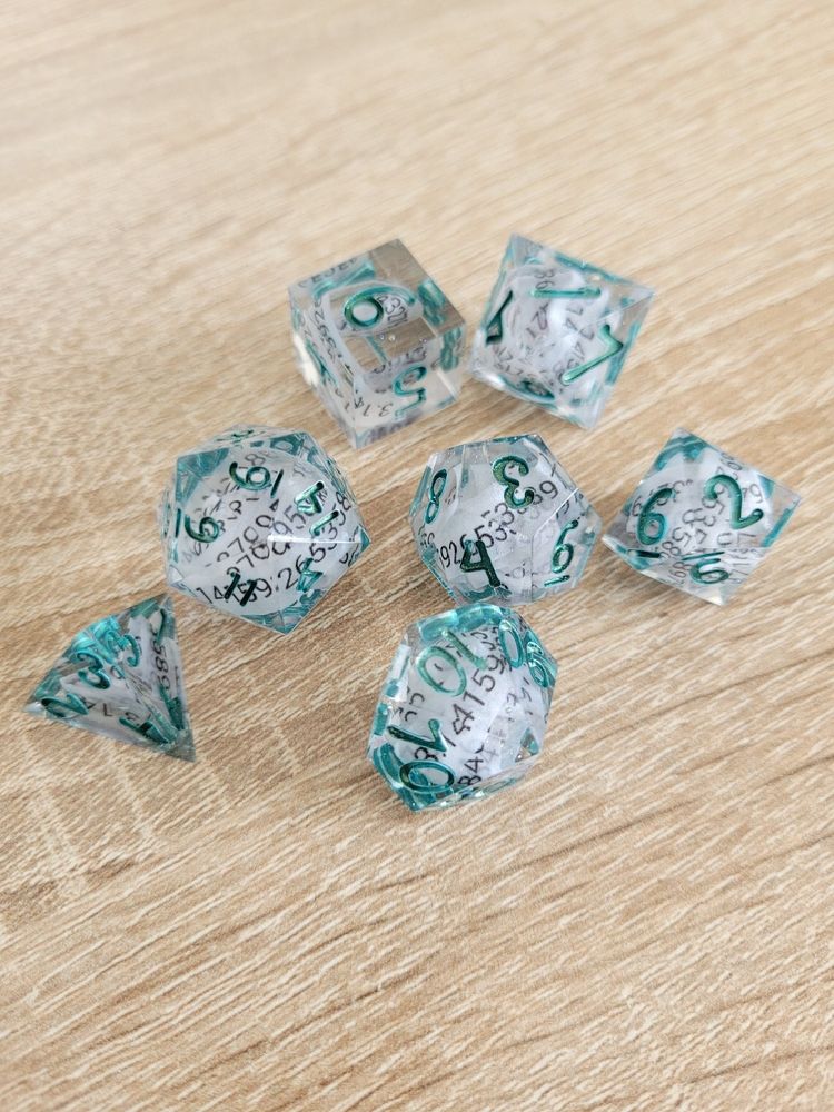 A clear polyhedral dice set, with turquoise inking, containing rolled up paper with the number pi on it. They sit on a light wooden surface.