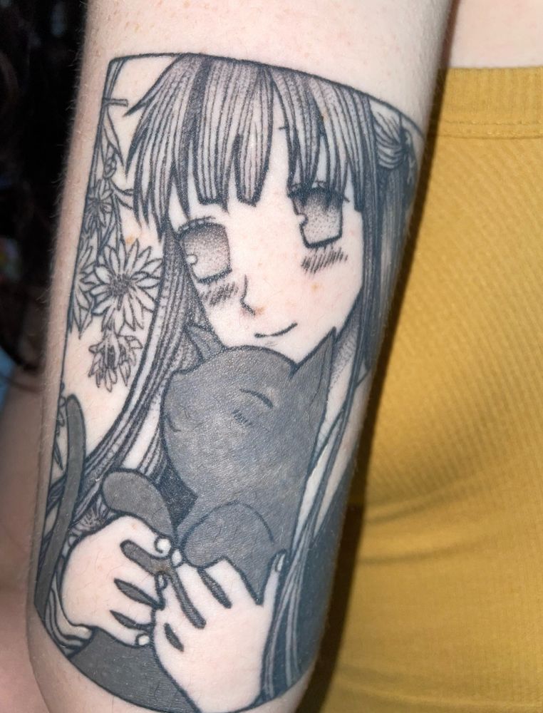 a tattoo of an anime girl (Tohru from Fruits Basket) holding a cat with flowers in the corner