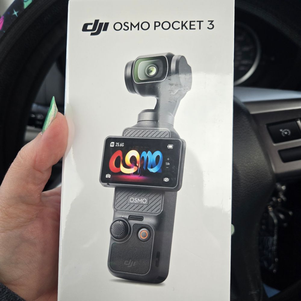 A hand holding a box with a dji osmo pocket 3 camera. They're in a car