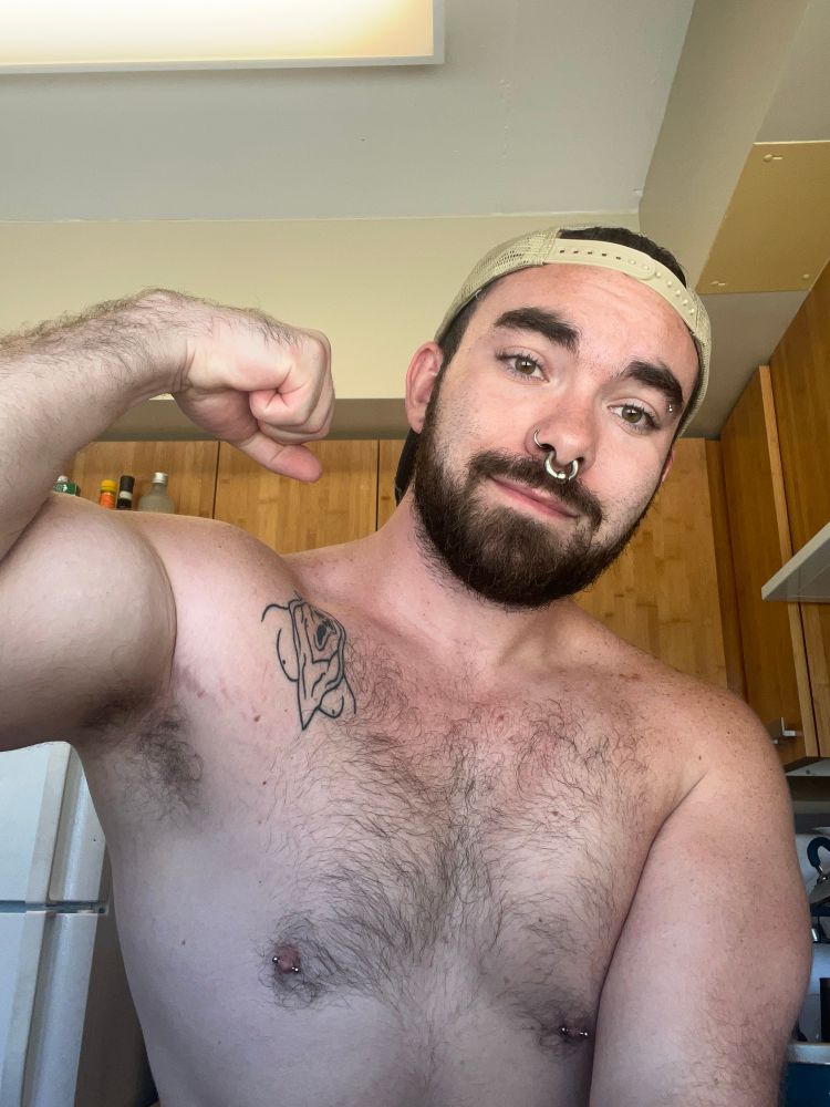 Person standing in the kitchen shirtless flexing their bicep and showing their armpit.