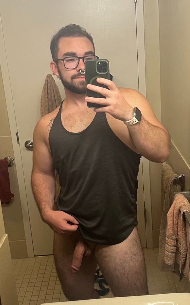 Mirror selfie in a bathroom with a muscular person in a top and no bottoms on with genitals showing. 