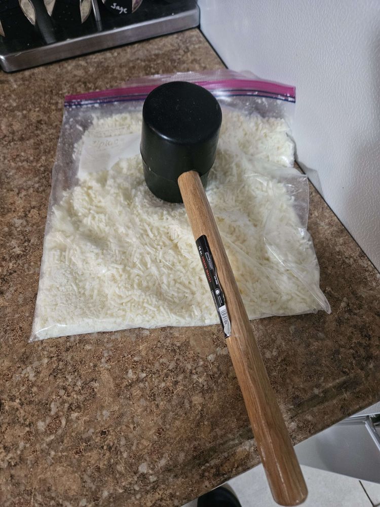 A bag of frozen shredded mozzarella that has been freshly hammered by a rubber mallet.