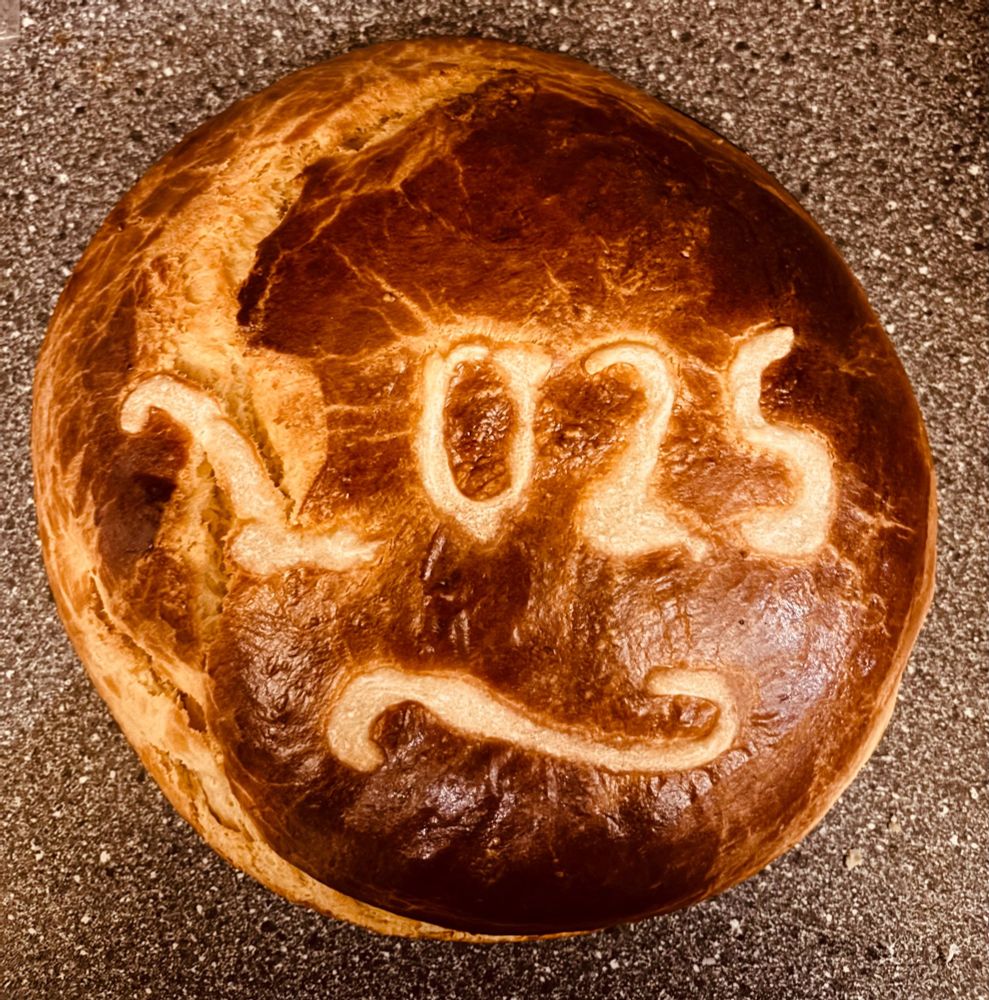 A top down photo of a vasilopita (new year’s bread) with 2025 written on the top despite a crack down the left hand side) 
