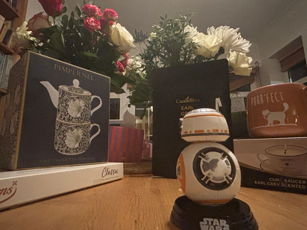 Photo of birthday gifts with flowers in vases in background, a posh tea pot set, and a model of BB8 in foreground 