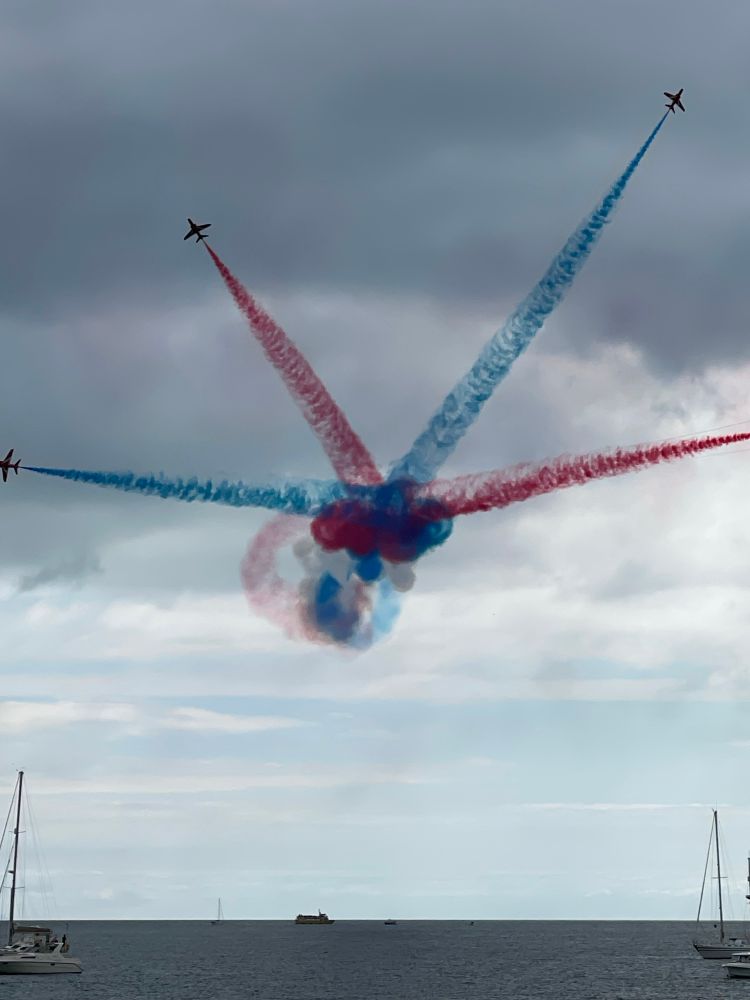 Photo of a trail from planes flying a star bust pattern.  Four coloured trails angle out from a central point, alternating blue and red. 