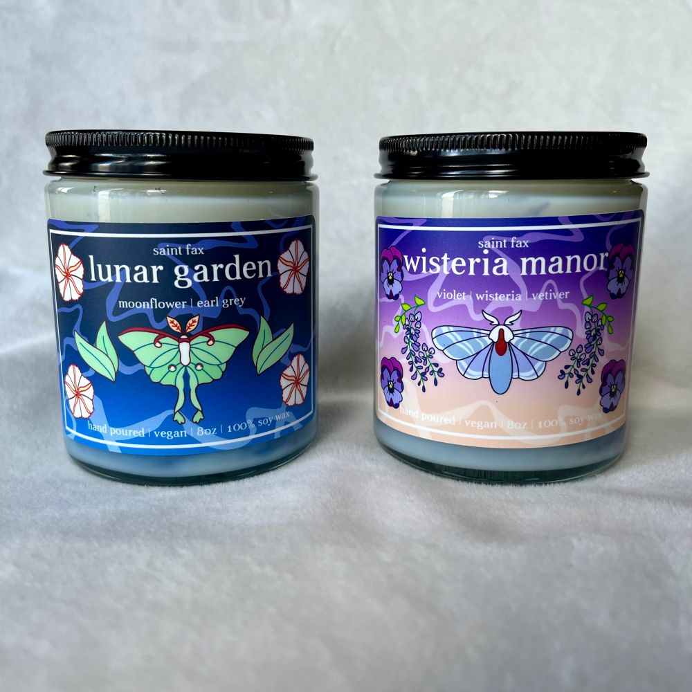 Two jarred candles with black lids on a white background. The candle on the left has a blue label with an illustration of a Luna moth surrounded by tea leaves and moonflowers. The candle on the right has a purple and champagne label with an illustration of a tolype moth surrounded by wisteria vines and violets. 

The left label reads: 

saint fax
lunar garden
moonflower | earl grey
hand poured | vegan | 8oz | 100% soy wax

The right label reads: 

saint fax
wisteria manor
violet | wisteria | vetiver
hand poured | vegan | 8oz | 100% soy wax
