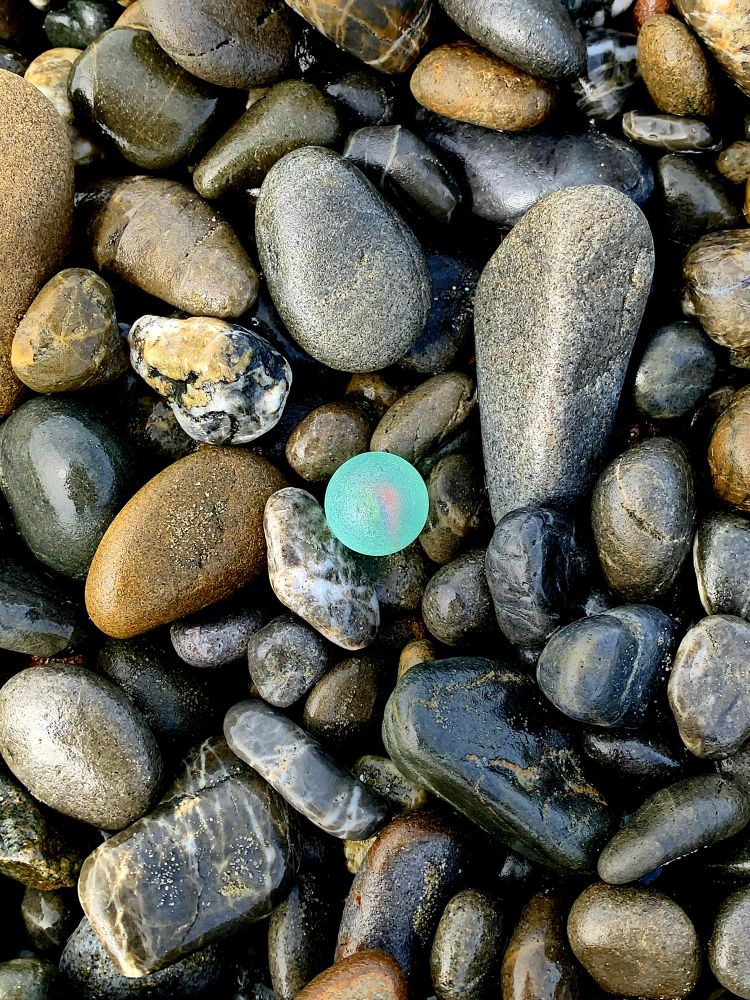 Close up of à light blue glass marble amongst wet pebbles on the beach. 