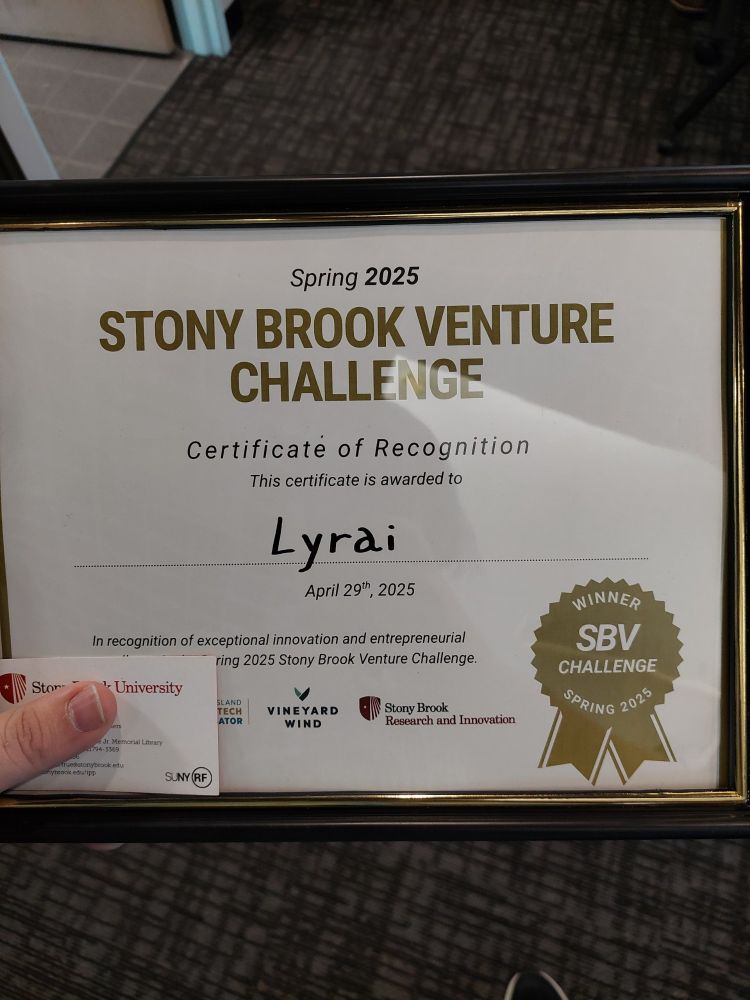 Alt text: A framed certificate of recognition for the Spring 2025 Stony Brook Venture Challenge is shown. It is awarded to "Lyrai" on April 29th, 2025, for exceptional innovation and entrepreneurial achievement. The certificate includes logos for Long Island Innovation Hot Spot, Vineyard Wind, and Stony Brook Research and Innovation. A gold ribbon on the right reads “Winner SBV Challenge Spring 2025.” A person's hand is holding the frame, with part of a Stony Brook University business card visible in the lower left corner.

