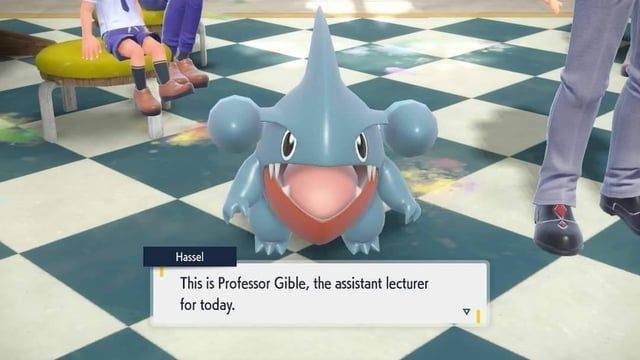 Captura de pantalla de un videojuego en la que aparece un Gible, un pequeño Pokémon azul con una gran boca, ojos expresivos y aletas laterales, sobre un suelo de baldosas en un aula. En el cuadro de diálogo, un personaje llamado Hassel presenta a "Profesor Gible, el profesor asistente de hoy". La imagen transmite una escena cómica al imaginar a Gible como docente.