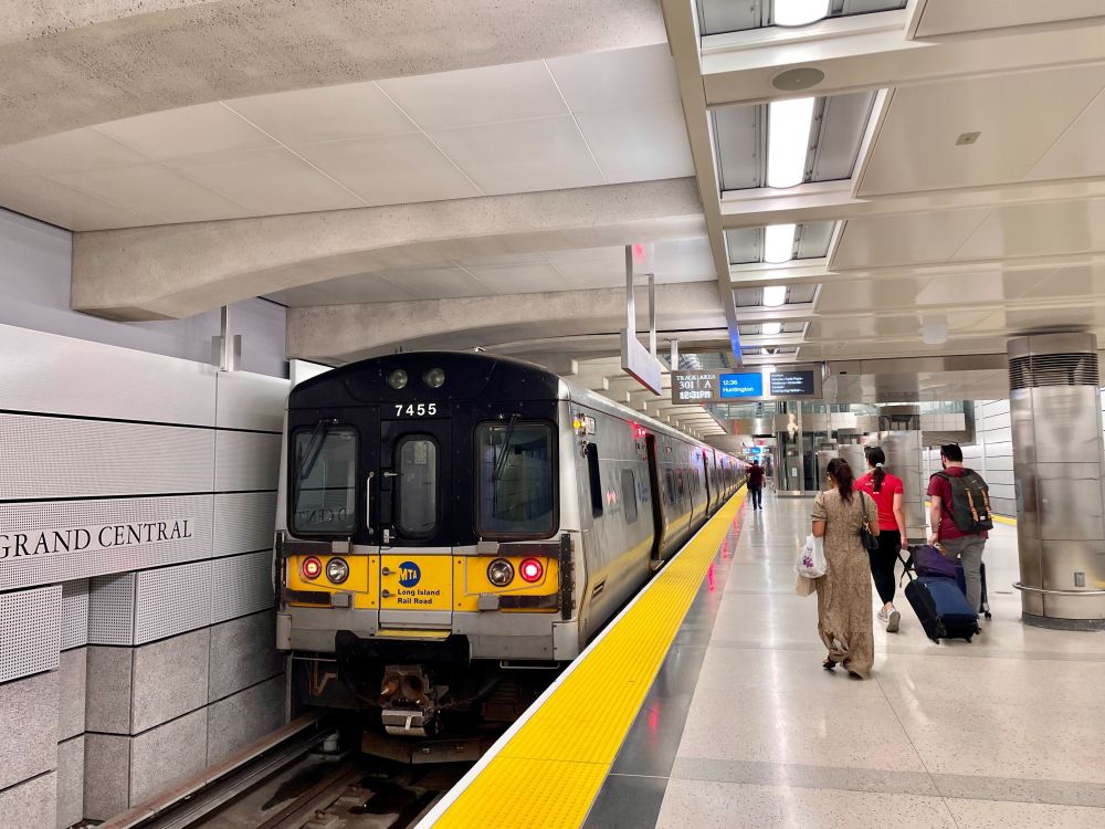 An LIRR train stationed at Grand Central Madison station, with people walking down the platform.