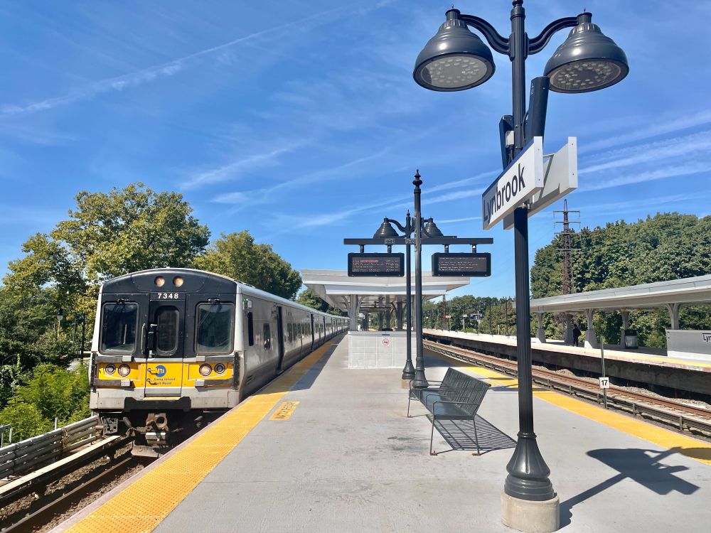 An LIRR train pulling into Lynbrook station on a sunny day. 