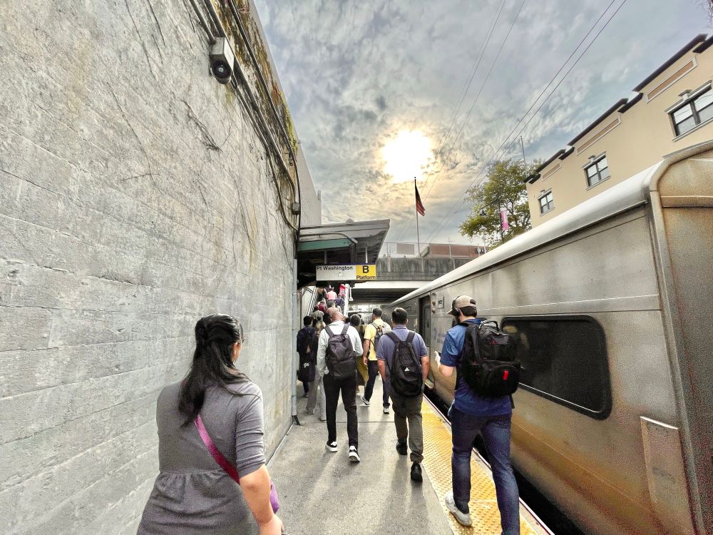 People walking down the platform after getting off a train at Bayside station on a partly cloudy day.