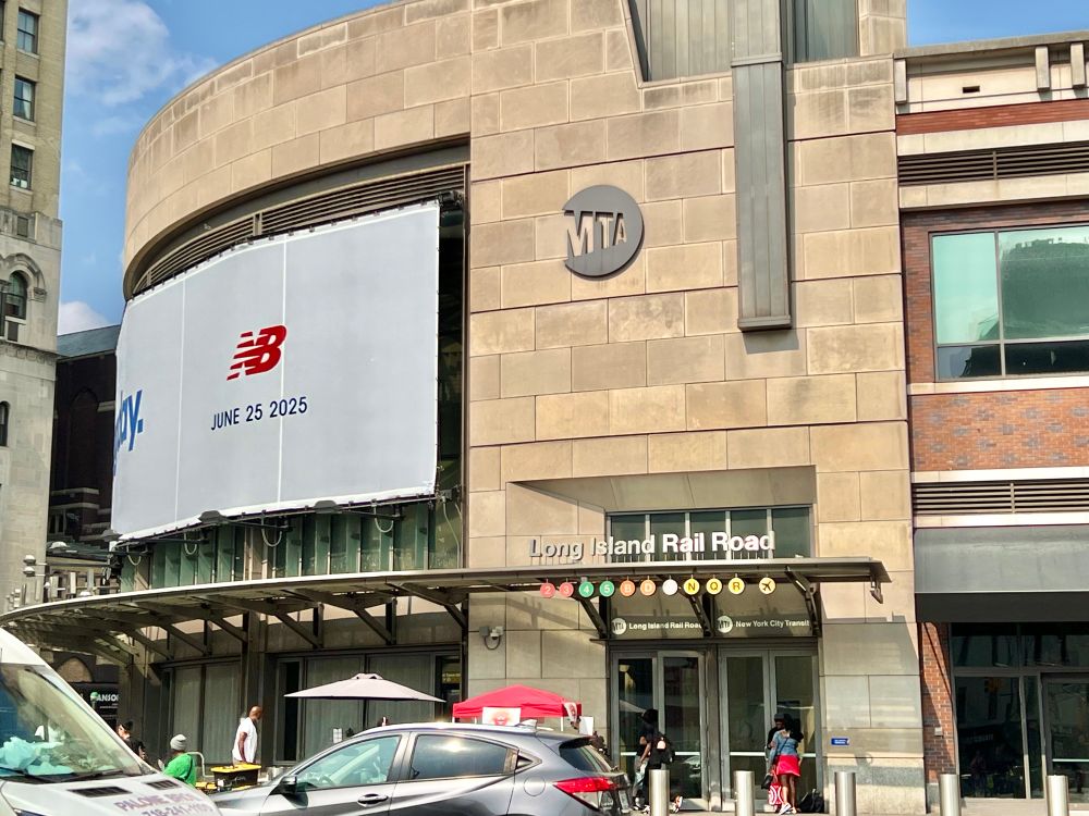 A modern-day photo of Atlantic Terminal, with cars parked outside and people walking past.   