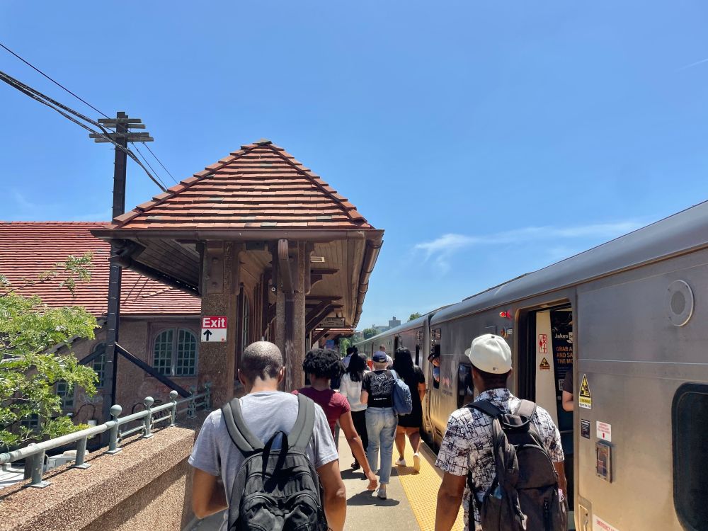 People walking down the Forest Hills platform on a sunny day, next to a stationed LIRR train.