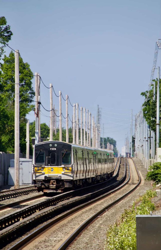 An LIRR train running along the tracks during the daytime.