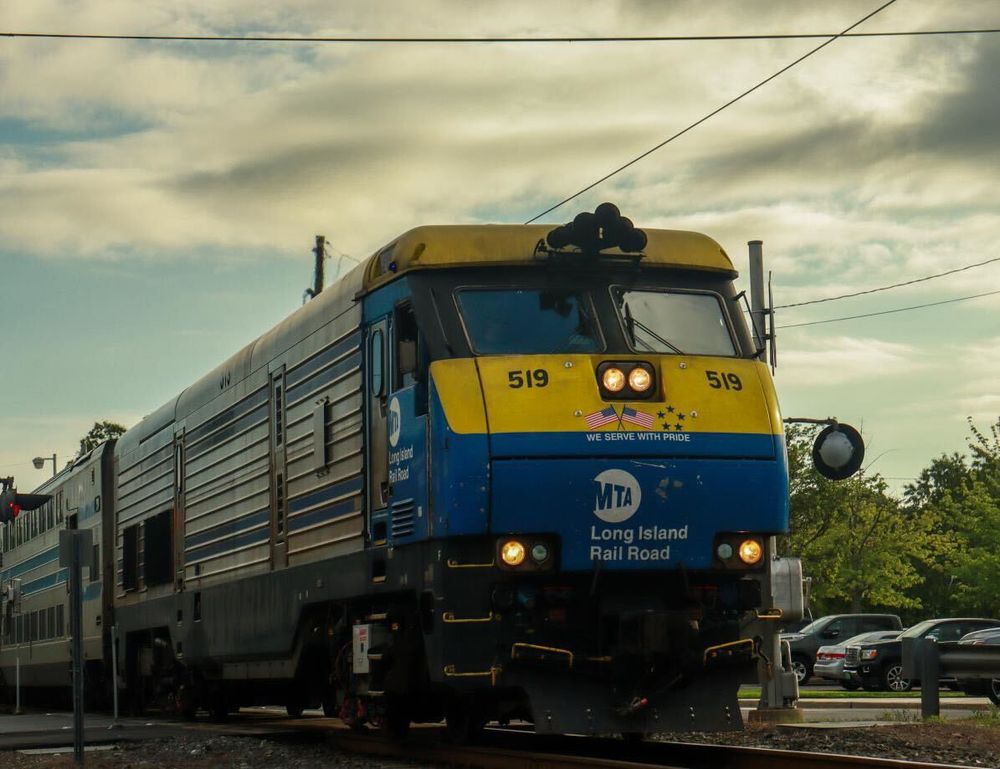 An LIRR diesel train running along the tracks at early sunset, on a cloudy day.