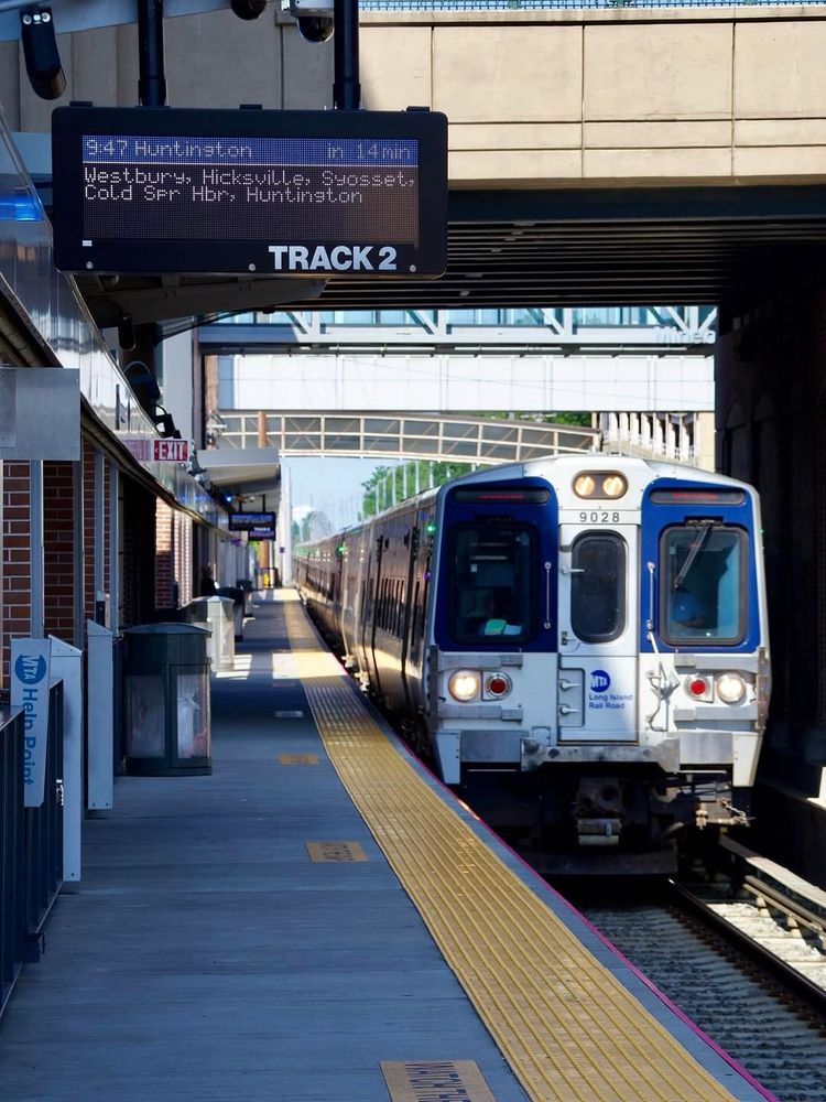 An LIRR M9 train pulling into Mineola station during the daytime. 