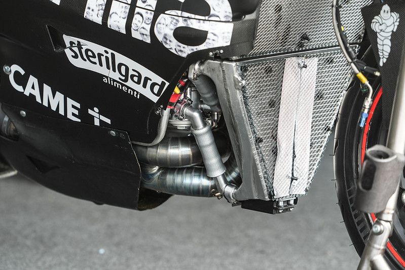 Here is the Aprilia RS-GP without the front bottom fairing fitted. You can see the two large exhaust headers, with a balance pipe just ahead of the fairing
The bottom radiator is the oil cooler. You can see the pipes running too and from the cooler, and what looks like an oil filter. The fact that there is duct tape on the oil cooler is a sign of how unseasonably cool it was at Sepang
