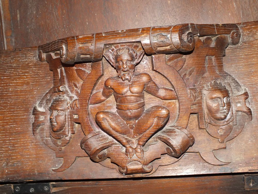 Mannerist misericord of a bearded faun inside strapwork flanked by two masks.