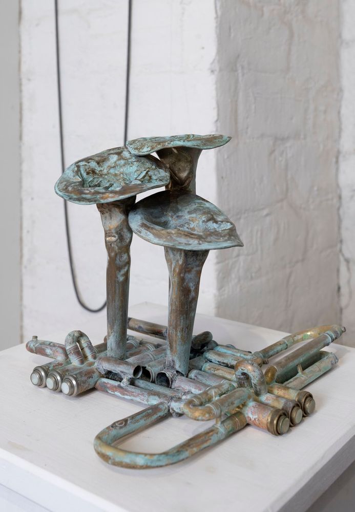 Three mushrooms made from three damaged trumpets on a white pedestal. White wall in the  background.
