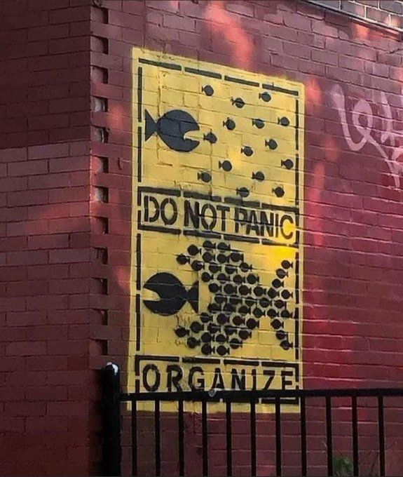 Mural of a big fish chasing little fish, black on yellow.
"Do Not Panic"
Small fish united to form the shape of a huge fish, chasing off the big fish.
"Organize"