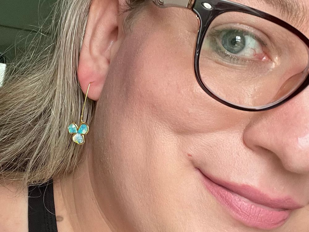 close-up of Suswave with beautiful raw-opal earrings! the opals shimmer blue, green, and white in bright gold fixtures.