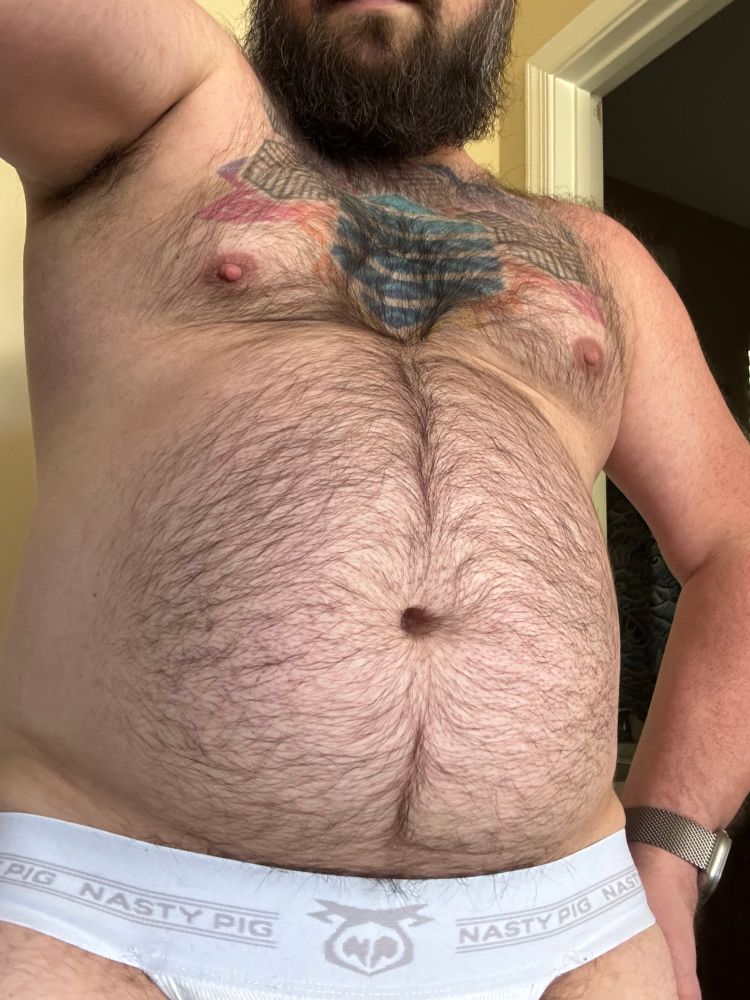 Me showing off my furry belly, chest, shoulders. More hair sticks out of the stained jockstrap I’m wearing. 