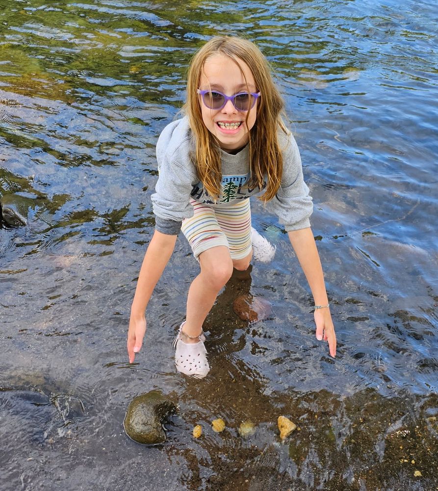 A girl in the river showing a line of rocks that looks like Pac-Man eating dots. 