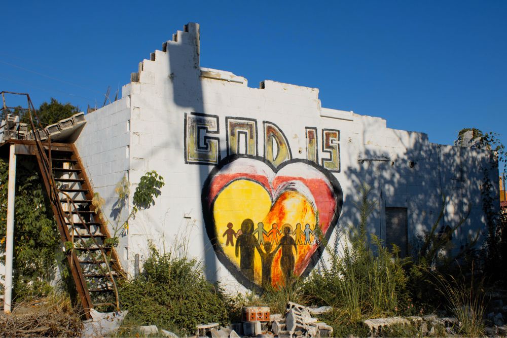 Photograph of graffiti on a burned and abandoned church, saying "GOD IS" above a heart with people holding hands inside it
