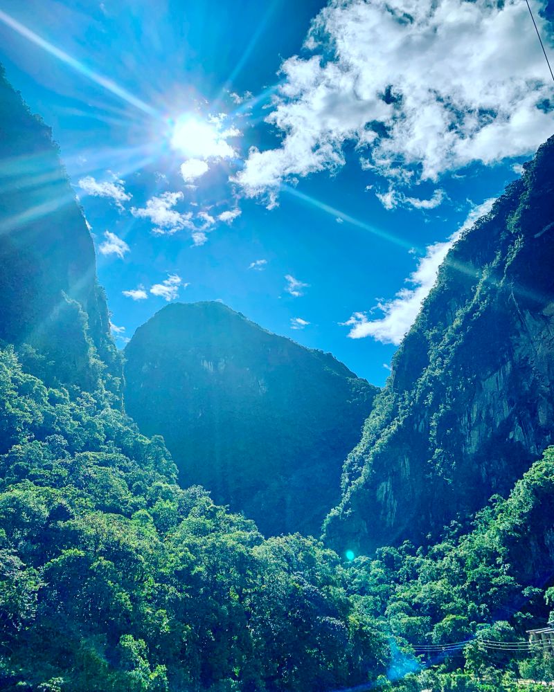 Tall green mountains with a sun flare. Bright blue sky with wispy clouds.