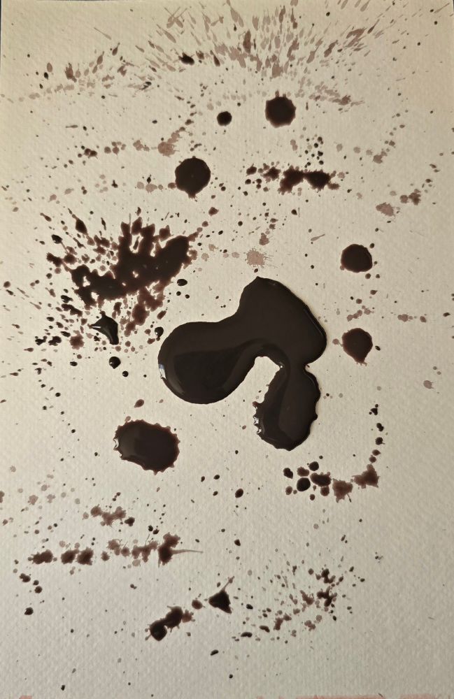 Watercolor ink blots in dark brown splattered on a white page. 