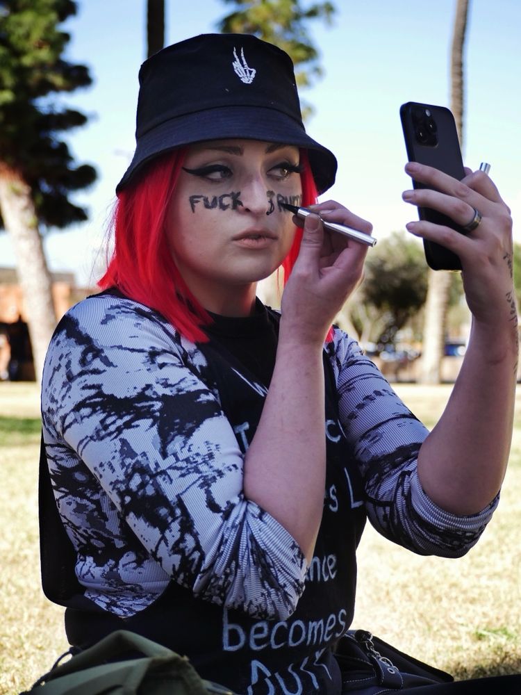 Protester writing “Fuck Trump” across face while sitting on the lawn of the Arizona State Capital 