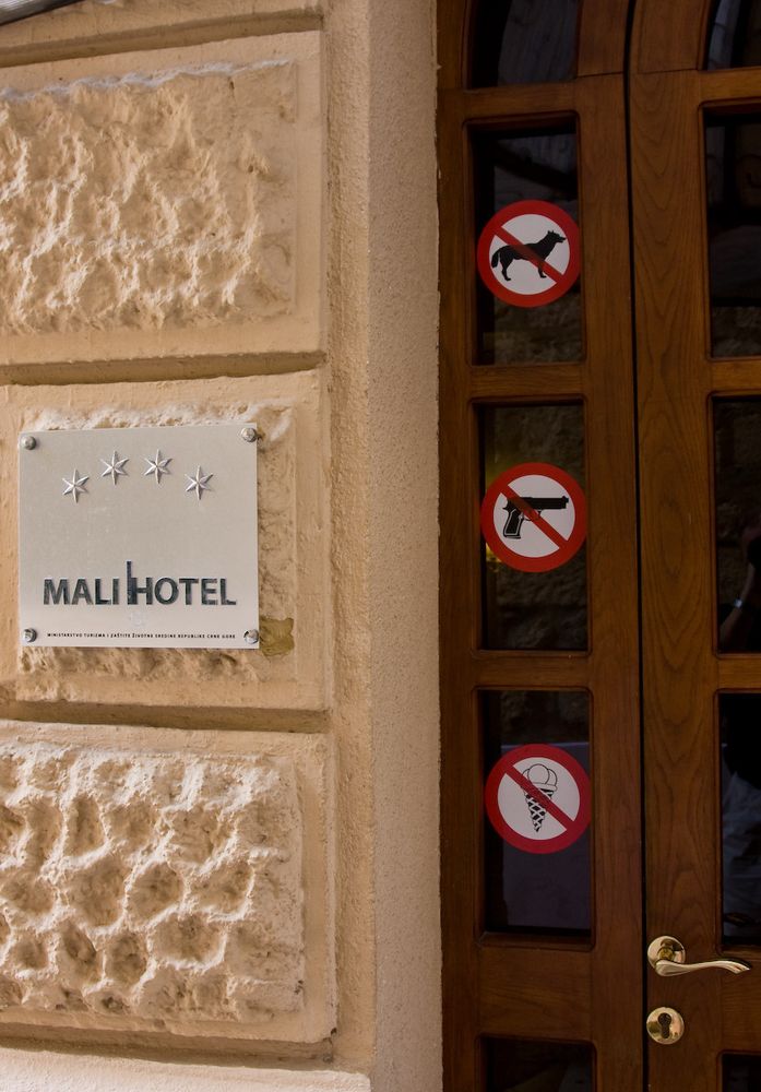 Hotel entrance with a sign showing "Mali Hotel" with four stars. On the door are three prohibition pictograms: no dogs, no guns, and no ice cream cones 