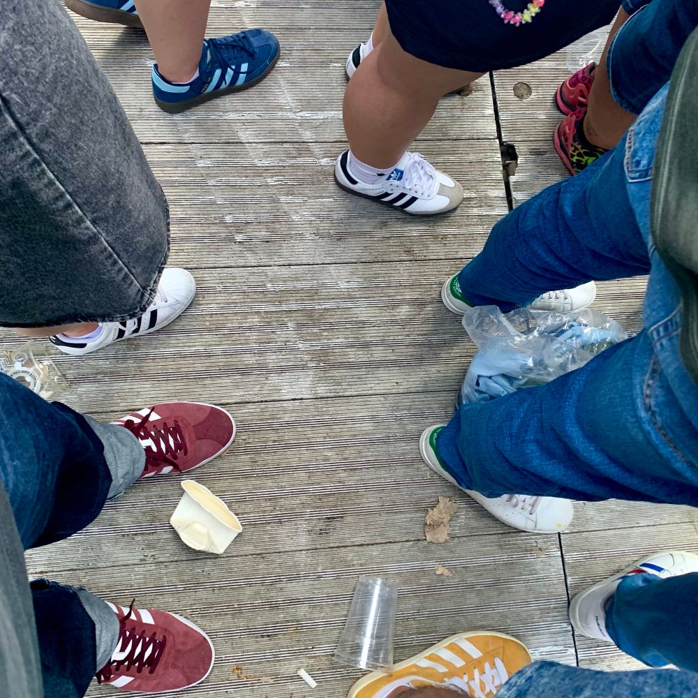 Blick zum Boden des Murrayfield Stadium beim Oasis-Konzert. Die Beine und Füße von 8 Leuten sind zu sehen, 7 davon tragen Adidas-Schuhe.