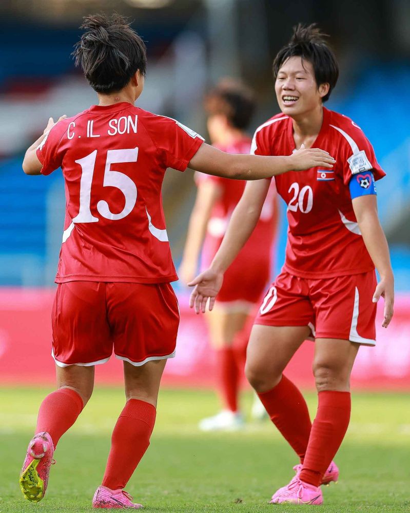 Duas atletas coreanas, de uniforme totalmente vermelho, se aproximam para um abraço de comemoração