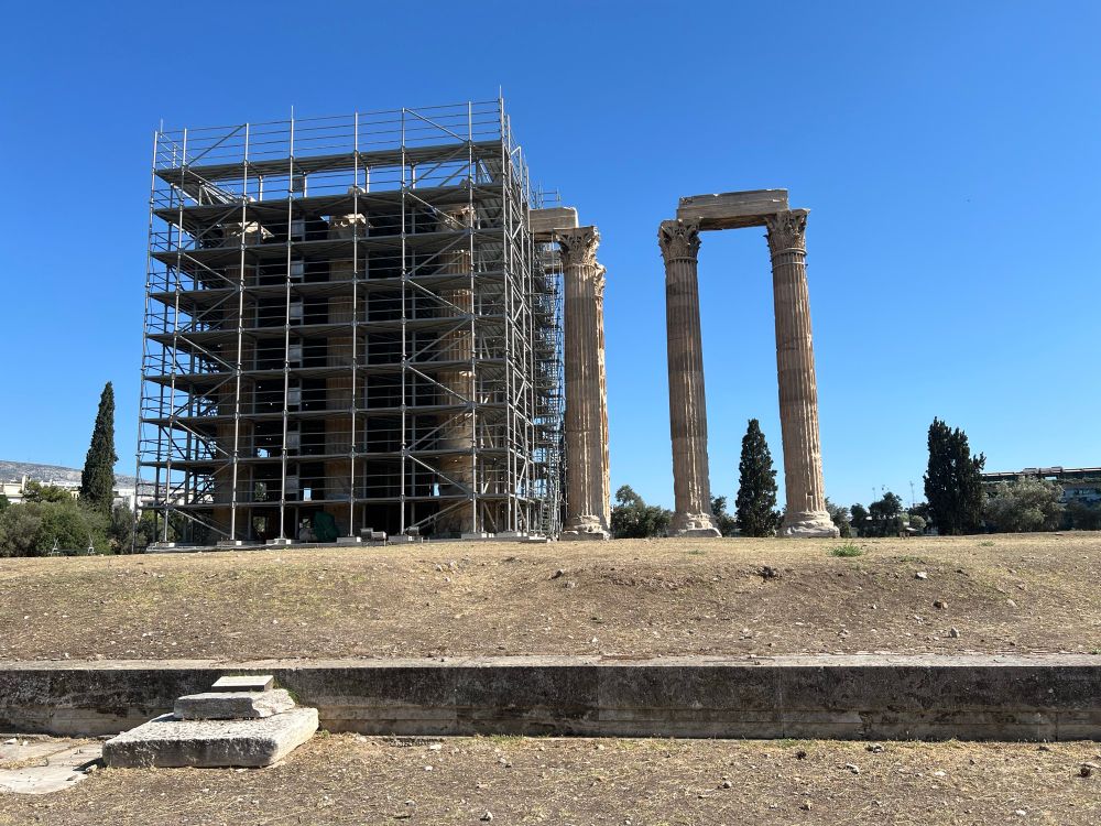 Two massive, Corinthian columns holding up a horizontal stone piece (I don’t know the correct word) situated next to about 10 similar columns surrounded by scaffolding.