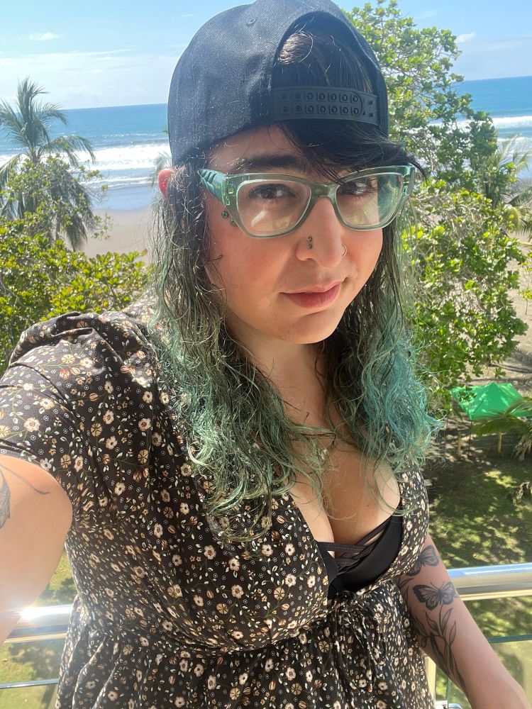 Olivia with curly green hair and a hat on backwards 