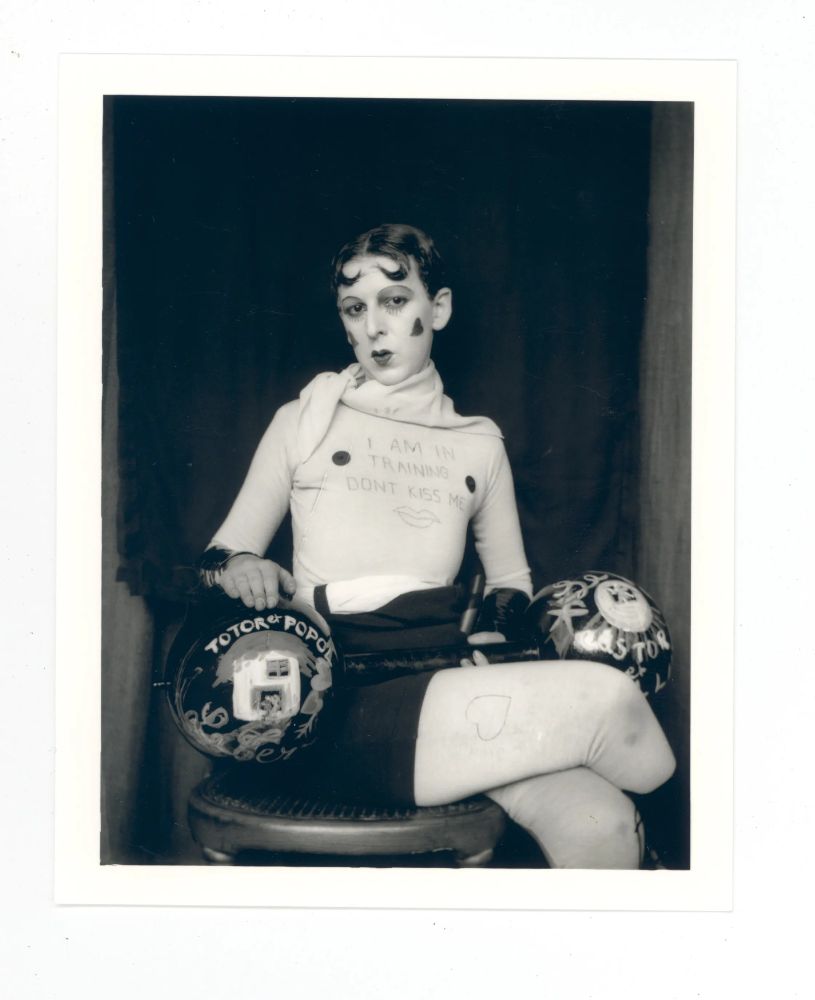 Claude Cahun with hearts on their face and I AM IN TRAINING DON'T KISS ME shirt