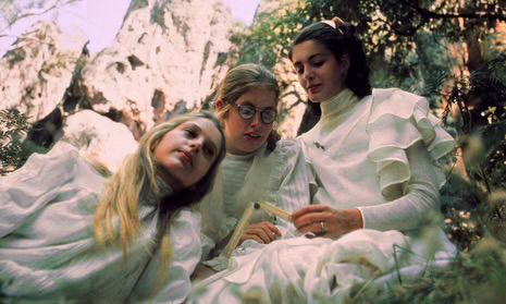 Three young white girls clad in white sitting among the trees with a promontory behind them. 
