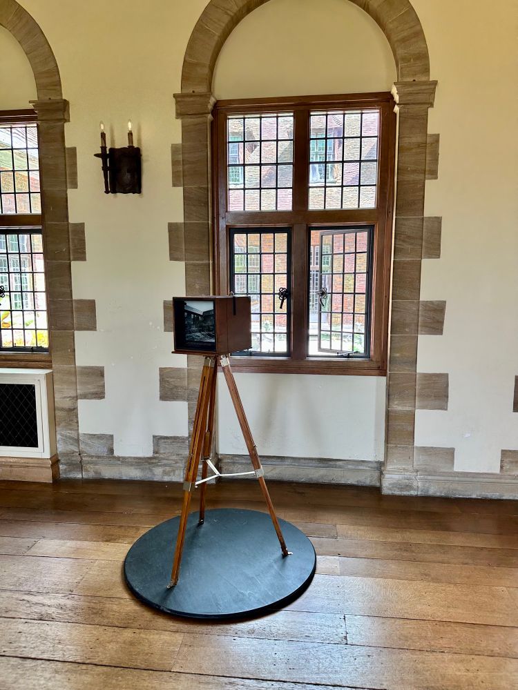 Another camera on wooden tripod, placed inside a room looking out the window towards courtyard