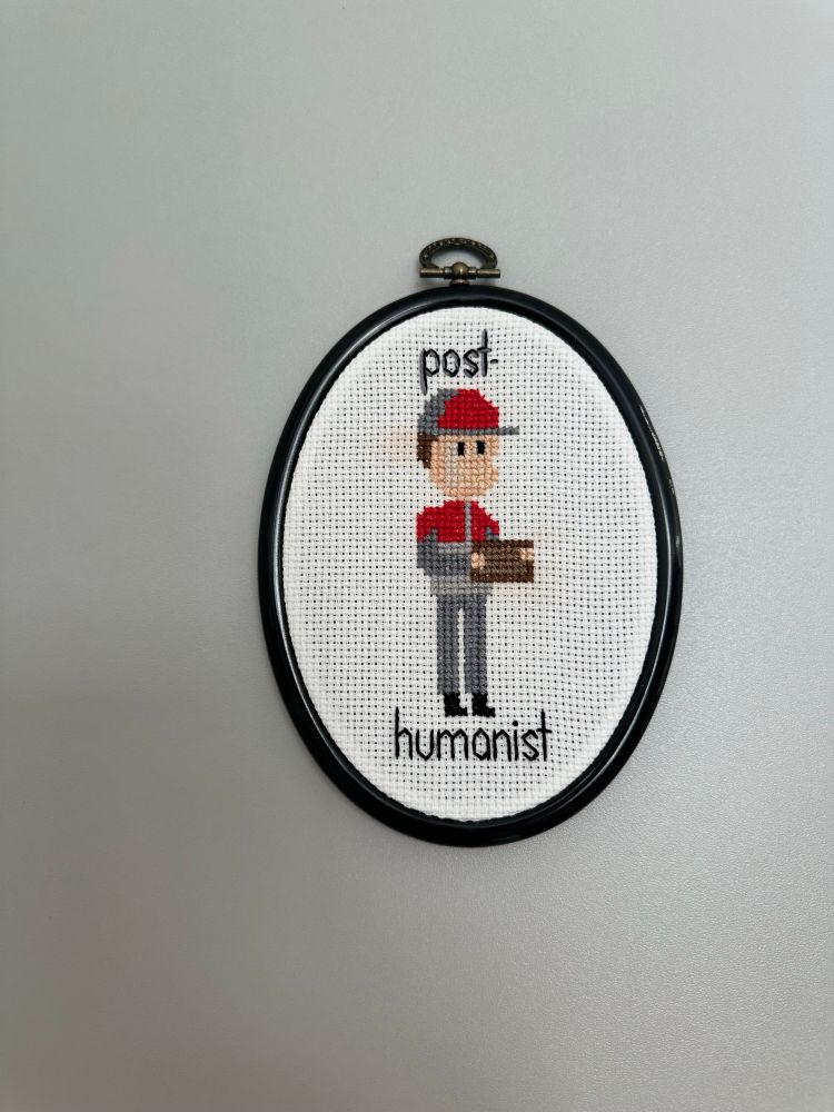 Framed oval embroidery of a person with the text «post-humanist»